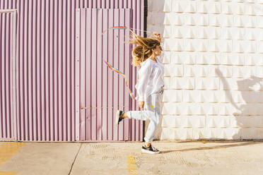 Woman doing rhythmic gymnastics in front of corrugated wall on sunny day - MGRF00763