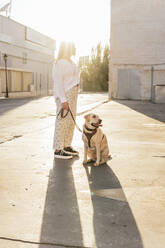 Frau stehend mit Hund an einem sonnigen Tag - MGRF00778