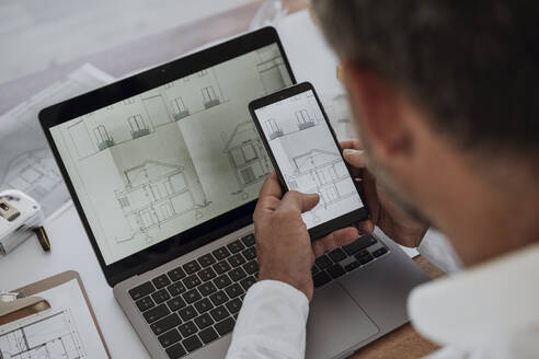 Hände eines Architekten, der eine Zeichnung auf einem Mobiltelefon im Büro analysiert - EBBF06073