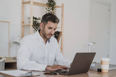Businessman using laptop at desk in office - EBBF06112