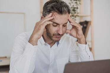 Stressed businessman sitting with laptop in office - EBBF06125