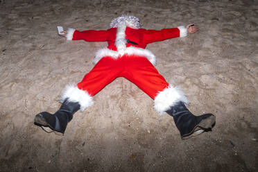Mann im Weihnachtsmannkostüm auf Sand am Strand liegend - GGGF00956