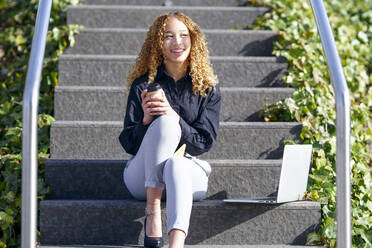 Glückliche Geschäftsfrau mit Kaffeetasse und Laptop auf einer Treppe sitzend - GGGF00957