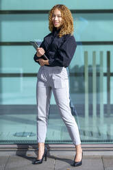 Smiling businesswoman standing with tablet PC on sunny day - GGGF00968