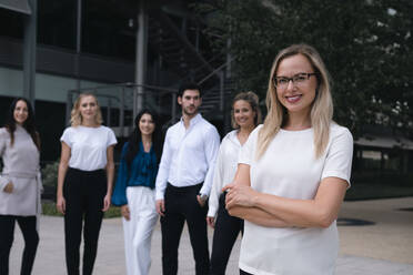 Smiling businesswoman standing with arms crossed in front of colleague at office park - AMWF00456