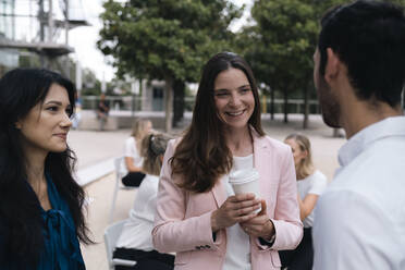 Businesswoman with coffee cup discussing with colleagues at office park - AMWF00463