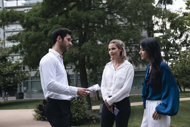 Young businessman discussing over documents with colleagues at office park - AMWF00472