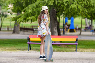 Glückliche junge Frau mit Skateboard im Park stehend - GGGF00983