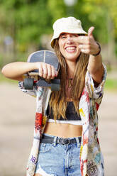 Fröhliche Frau mit Skateboard zeigt Mittelfinger - GGGF00984