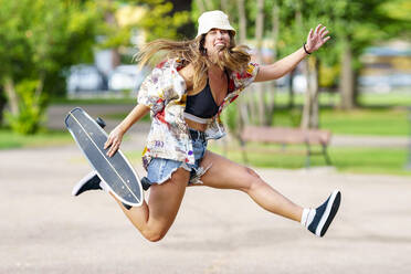 Unbeschwerte Frau mit Skateboard springt im Park - GGGF00985