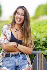 Happy young woman with arms crossed standing at park - GGGF00988