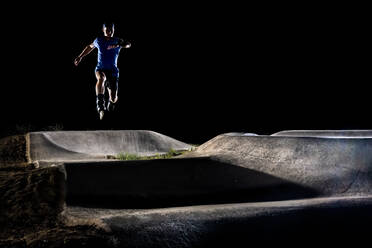 Man wearing inline skates jumping at skateboard park - STSF03474