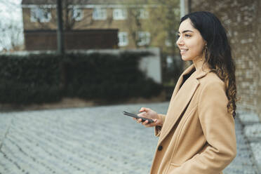 Lächelnde Frau mit Smartphone am Fußweg - AMWF00526