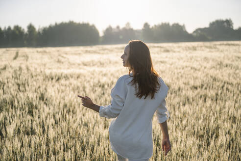 Frau zeigt auf Spaziergang im Kornfeld an einem sonnigen Tag - EYAF02096