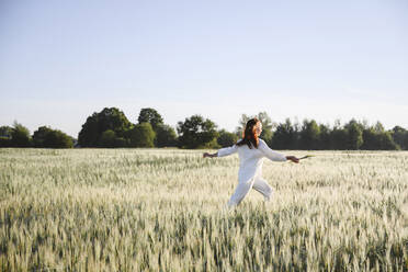 Carefree woman running in cornfield on sunny day - EYAF02098