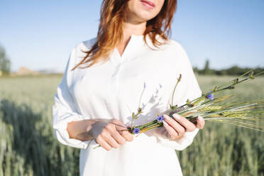 Frau mit Blumen im Kornfeld stehend - EYAF02099