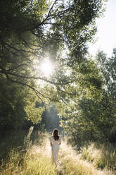 Woman wearing white dress walking in forest - EYAF02106