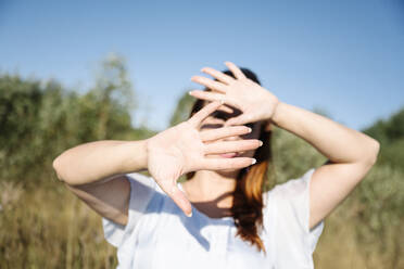 Frau bedeckt Gesicht an einem sonnigen Tag - EYAF02109