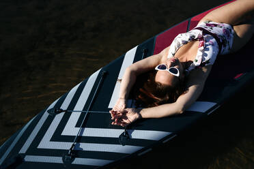Frau mit Sonnenbrille auf SUP-Board im See liegend - EYAF02113