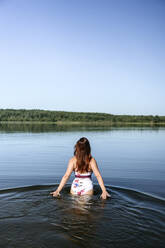 Woman walking in lake under blue sky - EYAF02115