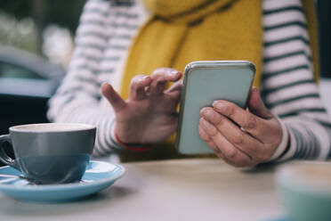 Frau benutzt Mobiltelefon mit Tasse am Tisch in einem Cafe - AMWF00532