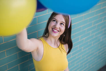 Lächelnde Frau mit Blick auf bunte Luftballons an der Wand - AMWF00565