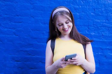 Beautiful woman using smart phone in front of blue wall - AMWF00574