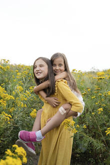 Mädchen nimmt Schwester huckepack, die auf einem Feld steht - LESF00011