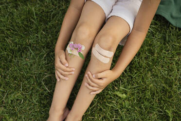 Mädchen mit Blumen, die mit einer Bandage an den Knien befestigt sind, sitzt im Park - LESF00026