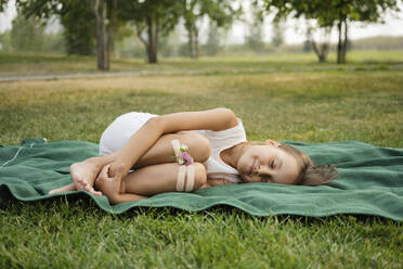 Girl with flowers attached to knees by bandage lying on blanket at park - LESF00028