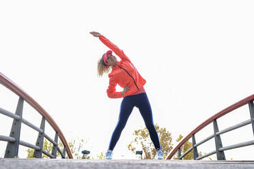 Glückliche Sportlerin beim Stretching auf einem Steg im Park - GGGF01010