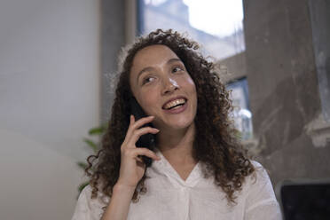 Glückliche Geschäftsfrau, die im Büro mit einem Mobiltelefon spricht - AMWF00582