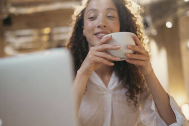 Lächelnde Geschäftsfrau mit Kaffeetasse und Blick auf den Laptop - AMWF00590