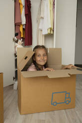 Smiling girl sitting in cardboard box at home - LESF00030