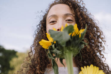 Junge Frau hält Sonnenblume vor das Gesicht - AMWF00602