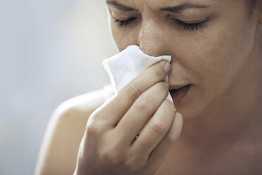 Ill woman blowing nose with tissue paper - AZF00431