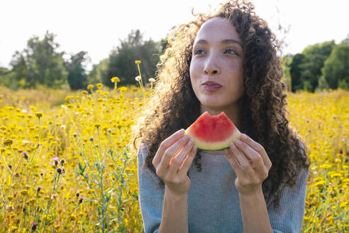 Nachdenkliche Frau mit Wassermelonenscheibe im Park - AMWF00607