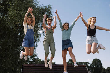 Happy friends jumping together in front of sky at park - AMWF00649