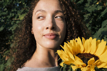Lächelnde schöne Frau mit Sonnenblume genießt das Sonnenlicht - AMWF00660
