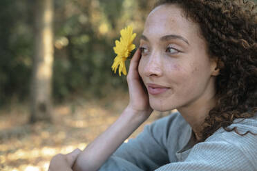 Thoughtful young woman with yellow flower at park - AMWF00661