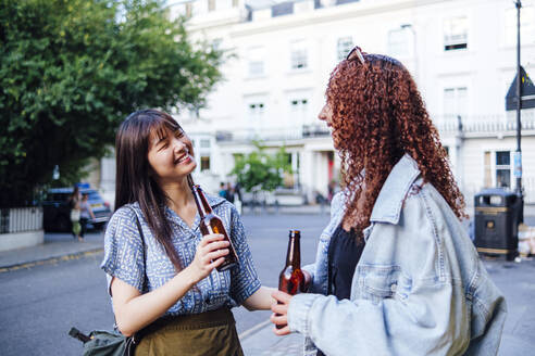 Glückliche junge Freunde mit Bierflaschen in der Stadt stehend - ASGF02806