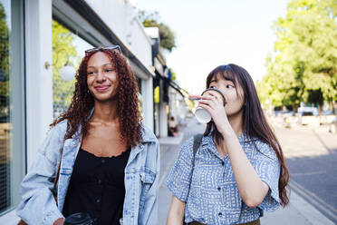 Smiling woman with friend drinking coffee at footpath - ASGF02824