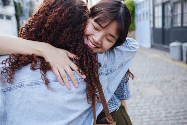 Smiling young woman hugging friend on street - ASGF02835