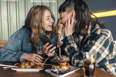 Loving lesbian couple with smart phone sitting at table in restaurant - JSRF02200