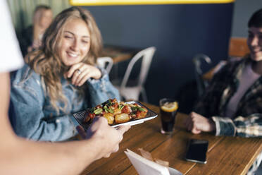 Hand of waiter serving food to lesbian customers in restaurant - JSRF02201