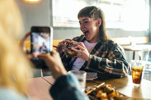 Junge Frau fotografiert Freundin mit Burger im Restaurant - JSRF02202