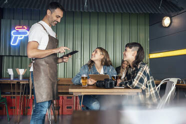 Zufriedener Kellner mit Tablet-PC, der die Bestellung eines Kunden im Restaurant aufnimmt - JSRF02203