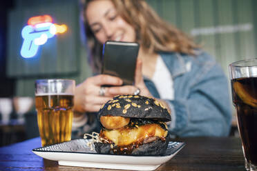 Junge Frau fotografiert Burger mit ihrem Smartphone im Restaurant - JSRF02205