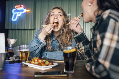 Junges lesbisches Paar beim Essen mit Stäbchen im Restaurant - JSRF02206