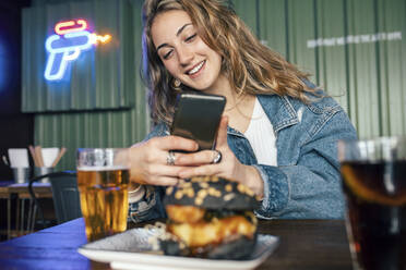 Glückliche Frau, die im Restaurant mit ihrem Smartphone Essen fotografiert - JSRF02207